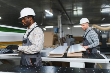 İki marangoz, bir mobilya fabrikasında mobilya üretimi için tahta kesen bir makineyle çalışıyor.