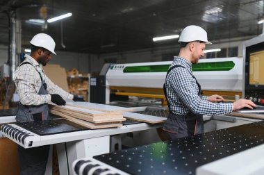 Mobilya fabrikasında ahşap ve modern bir cnc makinesiyle çalışan iki marangoz mobilya parçaları üretiyor.