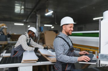 İki marangoz bir mobilya fabrikasında ahşap ve bilgisayar sayısal kontrol makinesiyle çalışıyor.