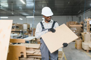 Ahşap panelde usta marangozlar, hareketli bir fabrika ortamında mobilya üretiminde ustalık ve hassasiyet gösteriyorlar.