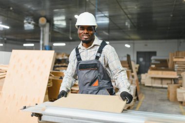Marangoz, yoğun bir mobilya fabrikasında titizlikle ahşap bir çarşaf şekillendiriyor, marangozluk, ustalık ve hassasiyet sergiliyor.