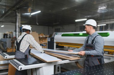 İki marangoz, cnc makinesinin yanında ahşap kalaslarda iş birliği yapıyor. Çalışan bir mobilya fabrikasında marangozluk yeteneklerini sergiliyorlar.