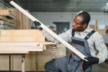 Afrika kökenli Amerikalı marangoz hareketli bir mobilya fabrikasında ahşap bir kalasın kalitesini inceliyor, birinci sınıf işçiliği garanti altına alıyor.