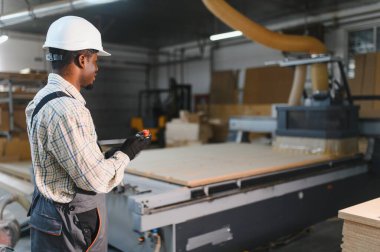 Marangoz, bir mobilya fabrikasında cnc ahşap yönlendirici çalıştırıyor, uzaktan kumandayla makineyi kontrol ediyor.