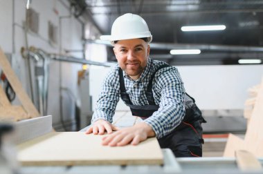 Marangoz, çalışkan bir mobilya fabrikasında çalışırken ahşap bir paneli inceliyor ve üretimde kalite ve hassasiyet sağlıyor.