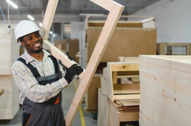 Gülümseyen marangoz mobilya fabrikasında ahşap çerçeve taşıyor, el işi ve endüstriyel üretim sergiliyor