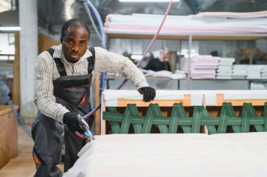 Marangoz mobilya fabrikasındaki kanepe montajında çalışıyor. Pnömatik zımba tabancasıyla ahşap çerçeveyi sağlamlaştırıyor.