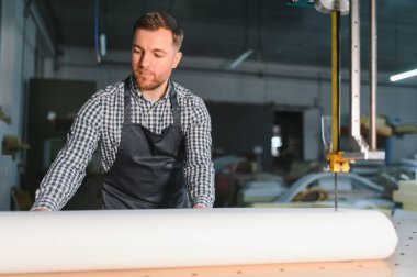 Marangoz, bir mobilya fabrikasında kumaş rulosu açıyor, kesin kesim ve uzman döşemelere malzeme hazırlıyor.