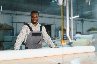 Marangoz bir mobilya fabrikasında kesim makinesi üzerinde çalışıyor, beyaz döşeme kumaşını kesmek için hazırlıyor.