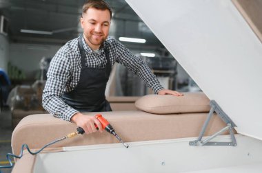 Marangoz maharetle bir kanepeyi pnömatik tornavidayla hareketli bir mobilya fabrikasında montajlıyor, el işi ve hassasiyet sergiliyor.