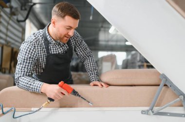 Marangoz bir mobilya fabrikasında kanepe monte ediyor. Pnömatik tornavidayı ustalıkla kullanarak üretim sürecini geliştiriyor.