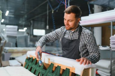 Marangoz pnömatik zımba tabancası kullanıyor, mobilya fabrikasında ahşap bir kanepenin döşemesini tamir ediyor.