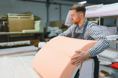 Mobilya fabrikasında kumaş ve köpük kullanarak kanepe monte eden yetenekli bir işçi. Cnc makineleri ve arka planda görünür ahşap malzemeler