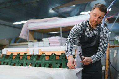 Marangoz, hareketli bir mobilya fabrikasında kanepe için kumaş kesiyor. Ustalıkla döşemelerde çalışıyor.