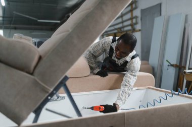 Bir mobilya fabrikasında kanepe monte etmek için elektrikli bir alet kullanan Afrikalı Amerikalı işçiler modern mobilya üretimindeki hassasiyet ve beceriyi sergilediler.