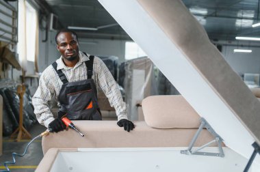 Marangoz, hareketli bir mobilya fabrikasında pnömatik bir tornavidayla kanepe monte ediyor.