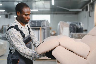 Marangoz, hareketli bir mobilya fabrikasında kanepe monte ediyor, marangozluk ve mobilya üretim sürecinde kendini adamışlık sergiliyor.