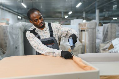 Marangoz, mobilya fabrikasındaki havalı zımba tabancasıyla maharetli bir şekilde koltukta çalışıyor, el işi ve hassasiyet sergiliyor.