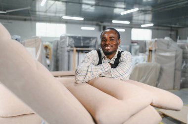 Bir mobilya fabrikasında kollarını kavuşturmuş gülümseyen Afrikalı bir Amerikan işçisinin portresi.