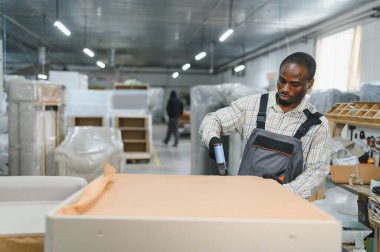 Marangoz, kumaşı zımbalamak için pnömatik çivi tabancası kullanarak bir kanepe fabrikasında mobilya montajlıyor.