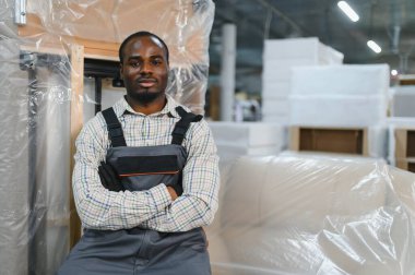 Afro-Amerikan marangozun portresi mobilya fabrikasında çapraz kollarla duruyordu.