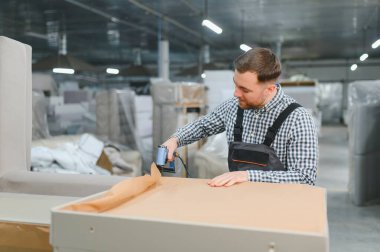 Marangoz bir mobilya fabrikasında ahşap mobilya monte ederken pnömatik zımba kullanıyor.