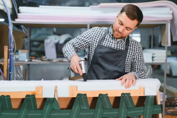 Marangoz, hareketli bir mobilya fabrikasında kanepe döşeyip, marifetli işçilik sergilerken pnömatik zımba tabancası kullanıyordu.
