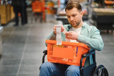Tekerlekli sandalyedeki bir adam süpermarketten alışveriş yaptıktan sonra alışveriş makbuzunu inceliyor, günlük hayatta bağımsızlığı ve kendine güvenini somutlaştırıyor.