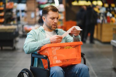 Tekerlekli sandalyedeki adam market fişini kontrol ediyor. Süpermarketteki toplam miktara şaşırmış.
