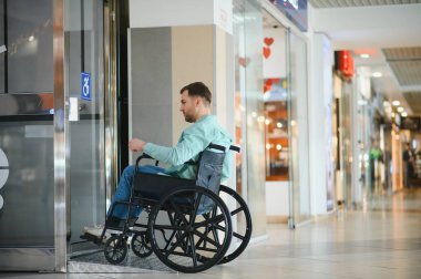 Tekerlekli sandalyedeki modern bir alışveriş merkezi asansöründen çıkan engelli, şehir hayatında bağımsızlık ve ulaşılabilir tasarım sergiliyor