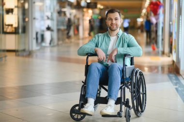 Tekerlekli sandalye kullanan kendine güvenen bir adam, modern bir alışveriş merkezinde geziniyor, hareket sorunu olan insanlar için ulaşılabilirlik ve kapsayıcılık gösteriyor.