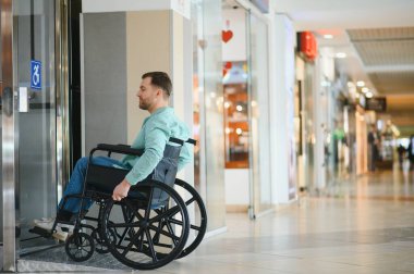 Engelli biri, tekerlekli sandalyedeki modern asansörden iniyor, kendine güveni ve bağımsızlığıyla canlı alışveriş merkezinde geziniyor.