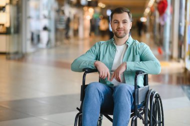 Tekerlekli sandalye kullanan mutlu bir adamın portresi, modern bir alışveriş merkezinde ücretsiz alışveriş deneyiminin tadını çıkarmak, engelliler için kapsayıcılığı ve erişilebilirliği teşvik etmek.