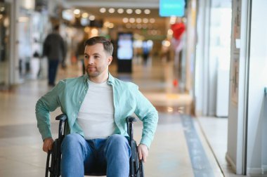 Tekerlekli sandalye kullanan sıradan bir adam alışveriş merkezi koridorunda hareket ediyor, boş zamanların ve ulaşılabilirliğin tadını çıkarıyor.