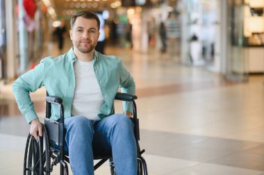 Tekerlekli sandalyedeki adam, yoğun bir alışveriş merkezinde, engelliler için hareket güçlüğü ve erişim sorunlarını vurguluyor.