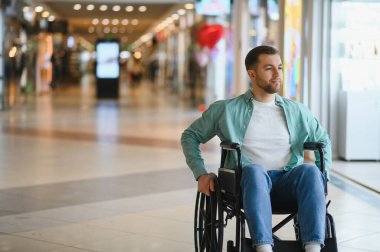 Alışveriş merkezinin koridorunda tekerlekli sandalye kullanan genç bir adam bariyersiz ortamın tadını çıkarıyor.