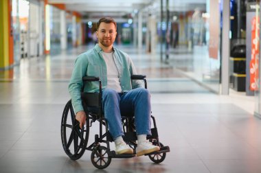 Müşteri tekerlekli sandalyeyle alışveriş merkezi koridorunda hareket ediyor, bariyersiz ortamda boş zamanın tadını çıkarıyor.