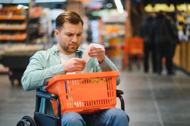 Tekerlekli sandalyedeki adam markette alışveriş yaparken market fişini kontrol ediyor.