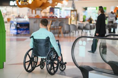 Alışveriş merkezinde asansörsüz ve rampasız, mimari engelli tekerlekli sandalye kullanan bir müşteri.