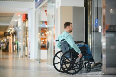 Müşteri tekerlekli sandalyeyle alışveriş merkezindeki asansöre biniyor, engelliler için erişim ve kapsayıcılığı temsil ediyor