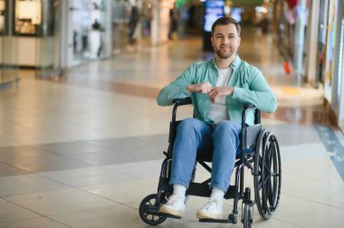 Tekerlekli sandalyedeki bir adam alışveriş merkezinde geziniyor, tekerlekli sandalye kullanıcıları için hareket güçlüğü ve erişim sorunlarını vurguluyor