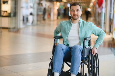 Bir alışveriş merkezinde tekerlekli sandalye kullanan mutlu bir adam, ulaşılabilirliğin ve bağımsızlığın tadını çıkarıyor.