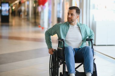 Tekerlekli sandalye kullanan engelli bir adam alışveriş merkezi koridorunda hareket ediyor, hareket sorunu olan insanlar için bağımsız yaşam ve ulaşılabilirliği temsil ediyor.
