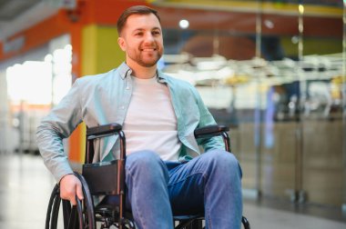 Paraplejisi olan mutlu bir adam alışveriş merkezinin koridorunda hareket eden tekerlekli sandalyeyle bariyersiz ortamın tadını çıkarıyor.