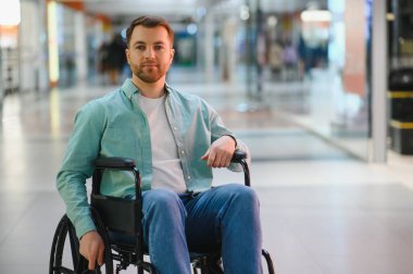 Tekerlekli sandalye kullanan genç bir adamın portresi, modern bir alışveriş merkezinde geziniyor, engelliler için erişilebilirlik ve kapsayıcılığı gösteriyor.