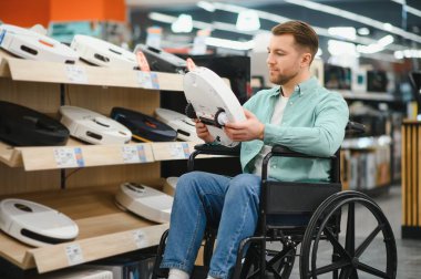 Tekerlekli sandalyedeki adam ev aletleri ve elektronik mağazasından robot elektrikli süpürge seçiyor ve yenilikçi temizlik çözümlerini keşfediyor.