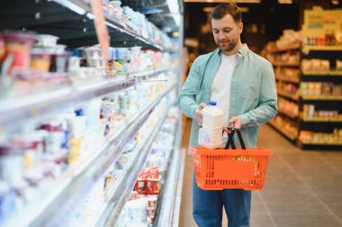 Man buying groceries, putting milk bottle in shopping basket, walking through refrigerated section of supermarket