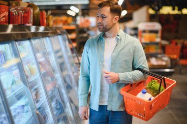 Elinde süt ve marul da dahil olmak üzere sebze sepeti olan bir adam süpermarketteki soğutulmuş bölüme göz gezdiriyordu.