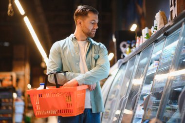 Müşteri elinde alışveriş sepetiyle marketteki dondurulmuş yiyecekleri seçiyor.