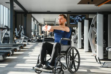 Spor salonunda tekerlekli sandalyede oturan engelli bir adam rehabilitasyon ve refah için egzersiz yapıyor.